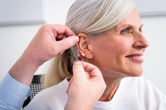 Eine Frau bekommt ein modernes Hörgerät angepasst und lächelt zufrieden dabei.